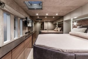 Interior of a luxurious Sunreef Yachts cabin with a large bed, mirrored walls, and a row of windows offering an ocean view.