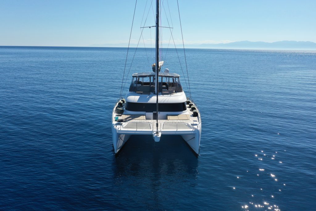 A Sunreef Yachts catamaran sails on a calm sea with a clear blue sky in the background.