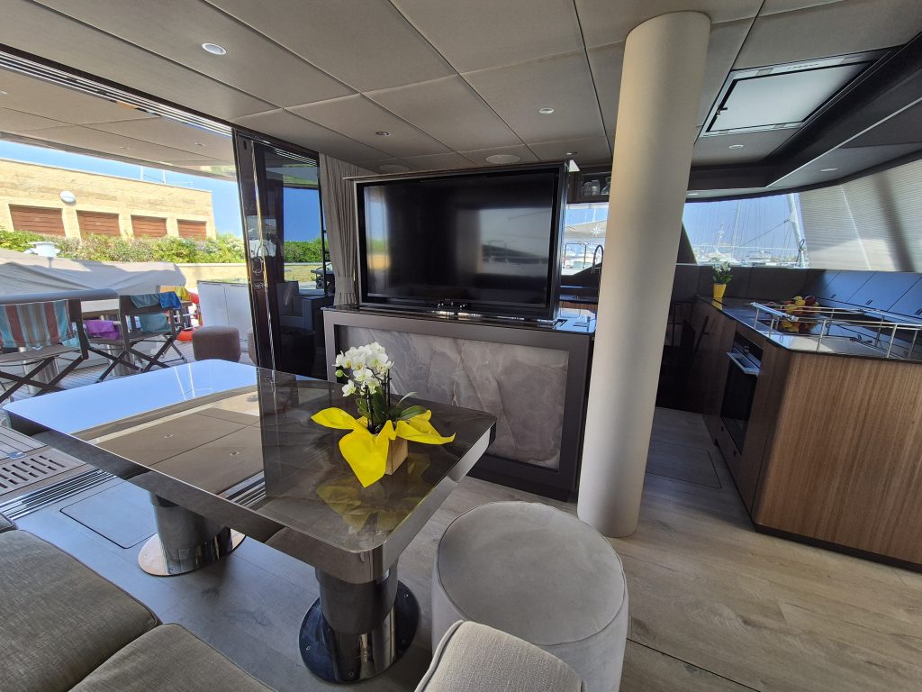 The interior of a luxury Sunreef Yachts catamaran features a modern dining area with a sleek table, decorated with a bouquet of white flowers and yellow cloth. The space is well-lit with ample natural light streaming from outside.