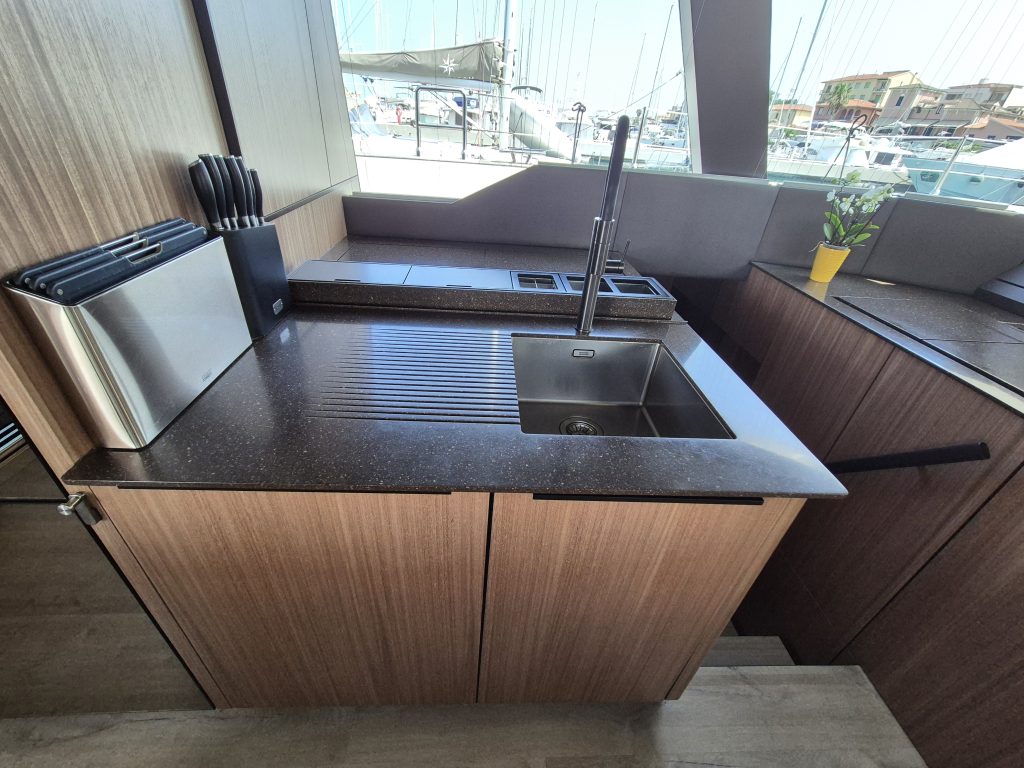Interior of a Sunreef Yachts kitchen with a modern sink, countertop, knife set, and a small potted plant near a window showing a marina.