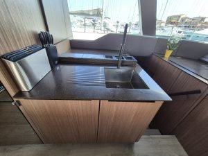 Interior of a Sunreef Yachts kitchen with a modern sink, countertop, knife set, and a small potted plant near a window showing a marina.