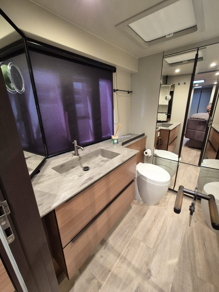 Interior of a Sunreef Yachts bathroom, featuring a modern design with a marble countertop, wooden cabinets, toilet, and large mirror.