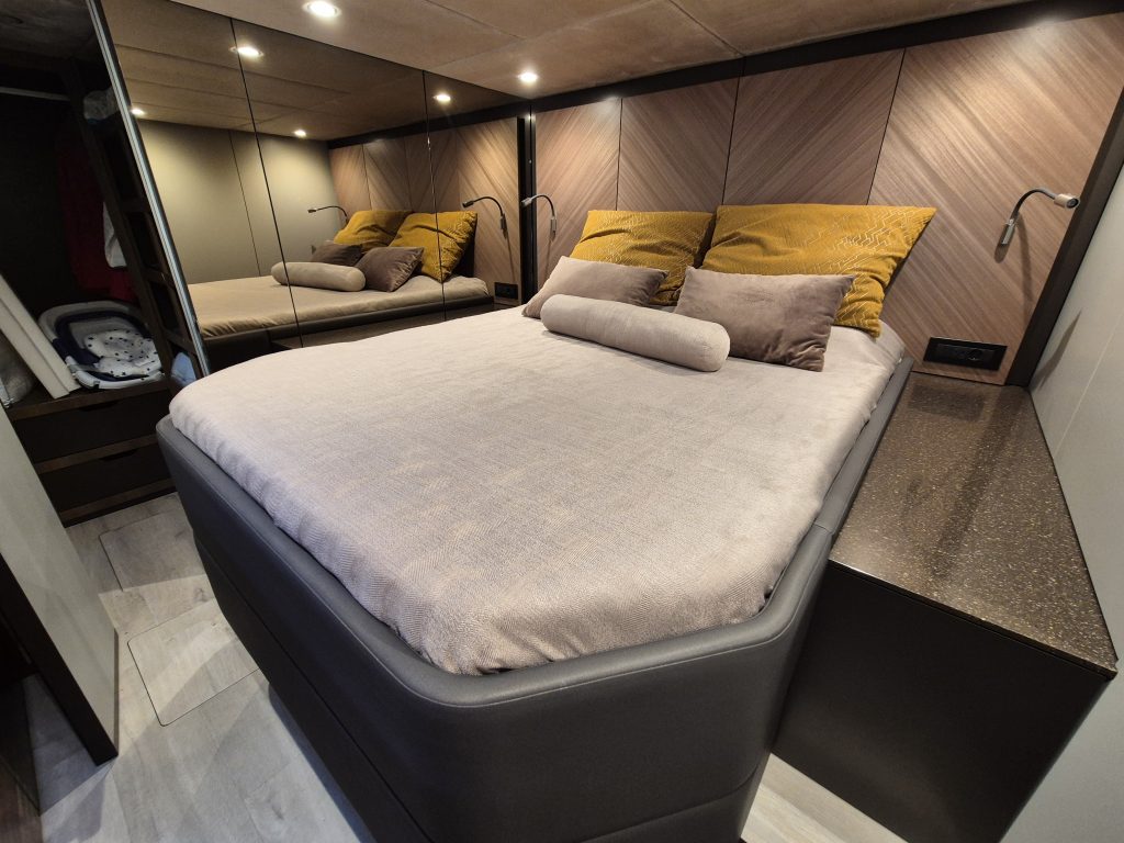 Interior of a Sunreef Yachts cabin featuring a cozy, neatly made bed with plush pillows and dark wooden accents.