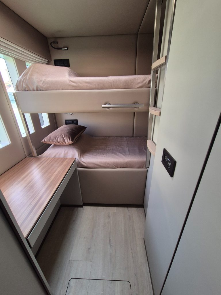 Interior of a room in a yacht by Sunreef Yachts, featuring two bunk beds with a small desk and window.