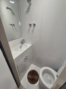 A compact modern bathroom on a Sunreef Yachts boat, featuring a white sink with cabinet, a mirror, and a toilet. Wall-mounted fixtures are visible.