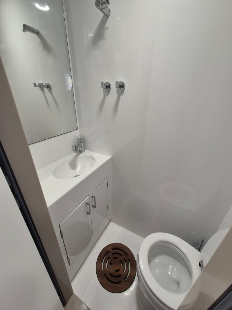 A compact modern bathroom on a Sunreef Yachts boat, featuring a white sink with cabinet, a mirror, and a toilet. Wall-mounted fixtures are visible.
