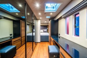 Interior of a Sunreef Yachts luxury yacht cabin with wooden flooring, a spacious bed, mirrors, and a skylight.