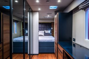 Interior of a luxury yacht cabin by Sunreef Yachts, featuring a neatly arranged bed with white and gray bedding, wooden paneling, and built-in cupboards with mirrored doors.