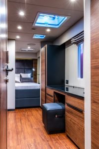 Interior of a cabin on a Sunreef Yachts vessel, featuring wooden flooring, a bed in the background, and cabinetry with a black countertop.