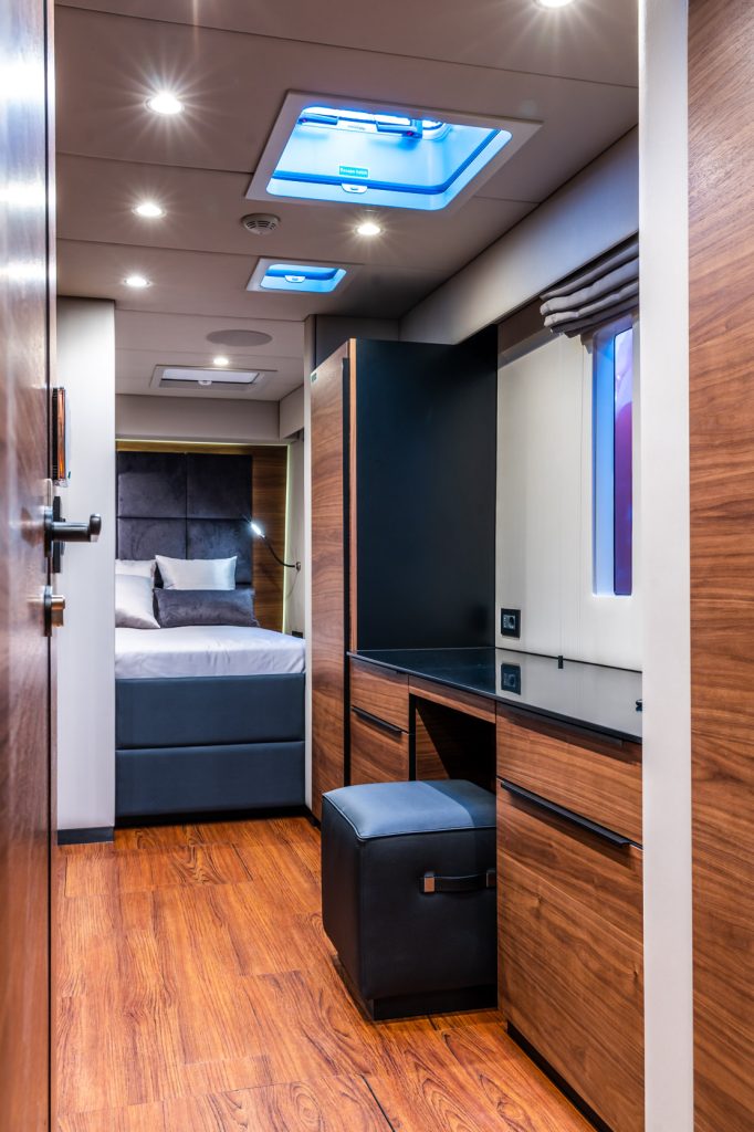 Interior of a cabin on a Sunreef Yachts vessel, featuring wooden flooring, a bed in the background, and cabinetry with a black countertop.