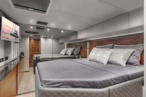 The interior of a luxurious yacht cabin by Sunreef Yachts, featuring a spacious bedroom with a large bed, elegant bedding, and modern lighting. A flat-screen TV is mounted on the wall, displaying an image of a yacht at sunset.