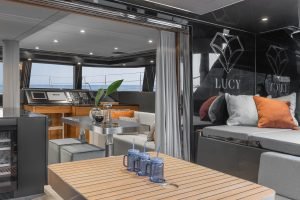 Interior of a luxurious Sunreef Yachts catamaran with modern furnishings, including a dining area with a wooden table and cushioned seating, and a view of the helm and exterior deck.