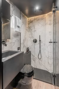 The image displays a luxurious bathroom interior from Sunreef Yachts. It features marble-patterned walls, a modern black faucet and shower head, a black toilet, and a sleek glass shower enclosure. A towel is neatly hanging on the wall.