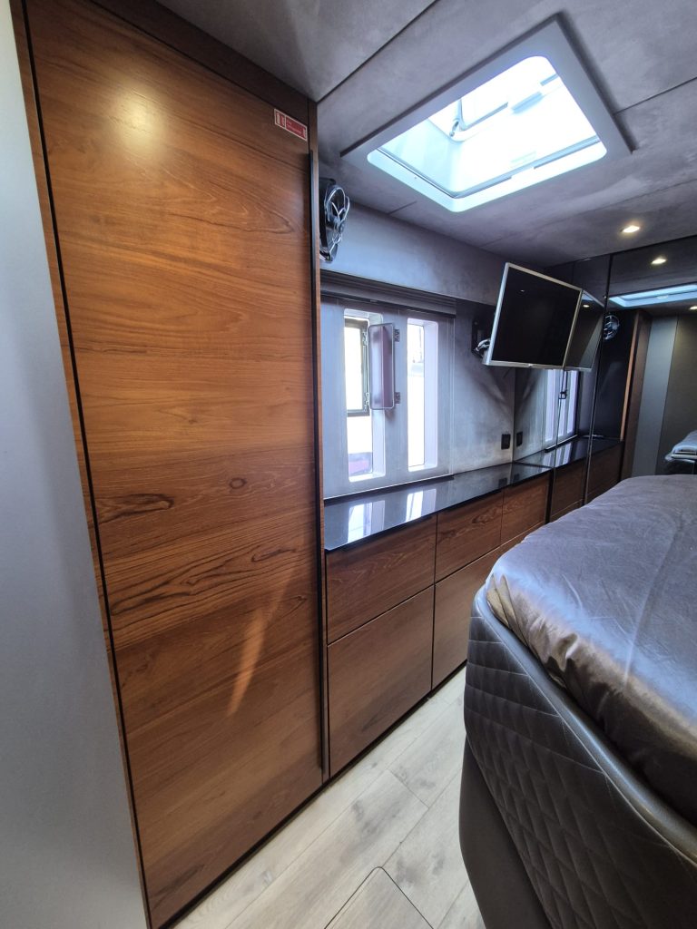 Interior of a luxurious Sunreef Yachts cabin featuring wooden paneling, a skylight, a mounted television, and a neatly made bed.