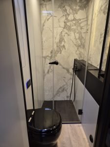 A luxurious bathroom from Sunreef Yachts features a black toilet, a glass-enclosed shower with marble-patterned walls, and modern fittings.