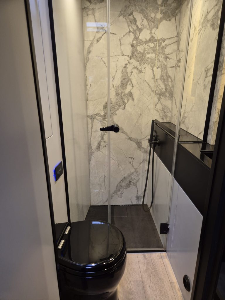 A luxurious bathroom from Sunreef Yachts features a black toilet, a glass-enclosed shower with marble-patterned walls, and modern fittings.