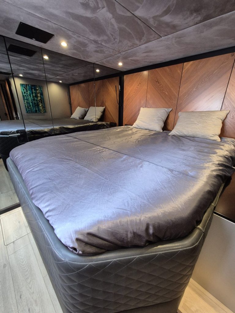 The bedroom inside a Sunreef Yachts vessel features a large, comfortable bed with a sleek design, wooden accent walls, and ambient lighting.