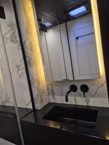 Interior of a luxurious Sunreef Yachts bathroom with black fixtures, a sleek black sink, marble-patterned walls, and ambient lighting.