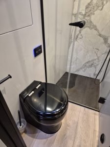 A luxurious bathroom on a Sunreef Yachts vessel features a sleek black toilet and a modern, glass-enclosed shower with beige and marble tile accents.