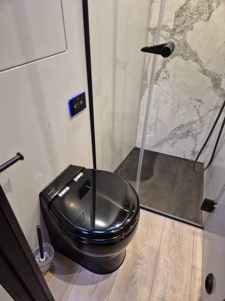 A luxurious bathroom on a Sunreef Yachts vessel features a sleek black toilet and a modern, glass-enclosed shower with beige and marble tile accents.