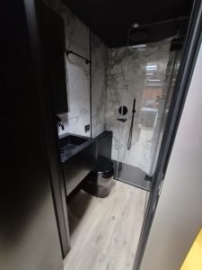 This image shows a modern bathroom in a Sunreef Yachts vessel, featuring a sleek, marble-accented shower, black fixtures, and a wooden floor.