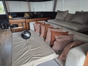 Interior of a luxury Sunreef Yachts catamaran, featuring a modern living area with a beige sofa adorned with patterned cushions. A black and white globe sits on a coffee table covered with a cloth. The helm station is visible in the background.