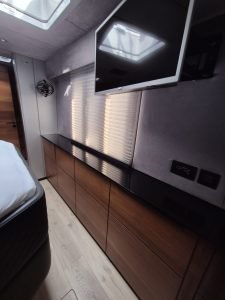 Interior of Sunreef Yachts with a modern design, featuring a sleek black countertop, wooden cabinets, a mounted television, and a large window covered by blinds.