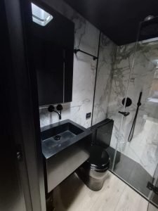 The image shows a modern bathroom on a Sunreef Yachts vessel, featuring marble-like walls, a sleek black sink, and a glass shower enclosure.