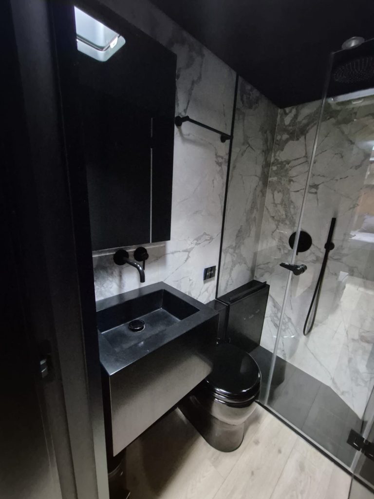 The image shows a modern bathroom on a Sunreef Yachts vessel, featuring marble-like walls, a sleek black sink, and a glass shower enclosure.