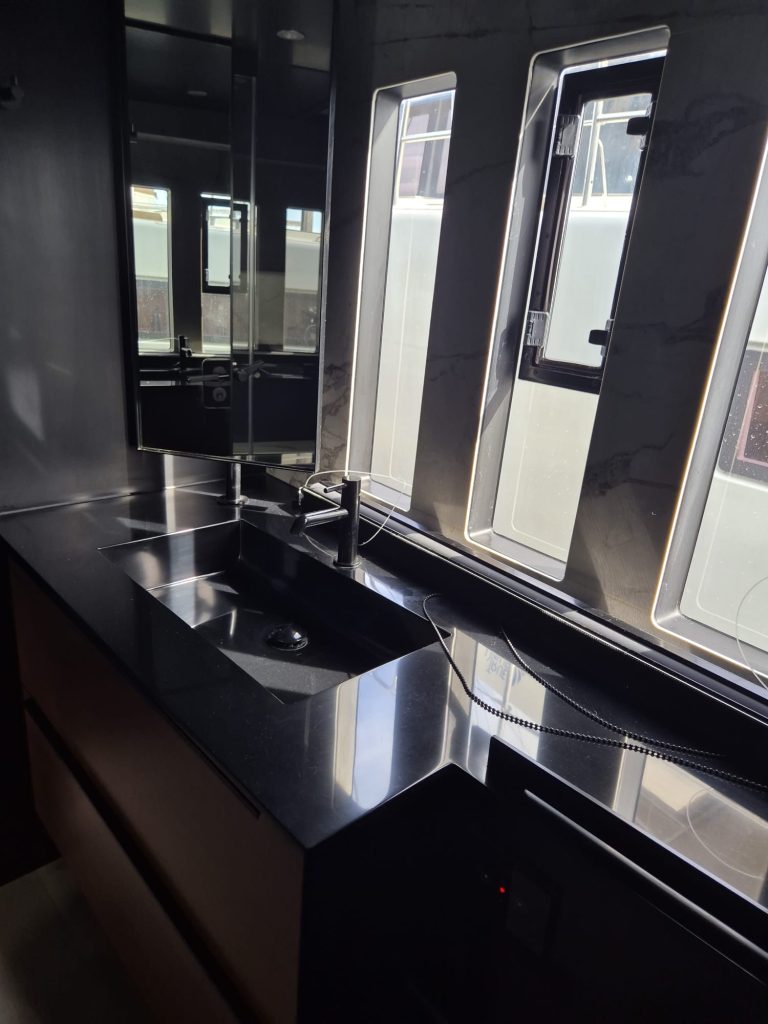 Interior of a Sunreef Yachts vessel, showing a modern kitchen area with a sleek black countertop and sink, illuminated by sunlight streaming through narrow windows.