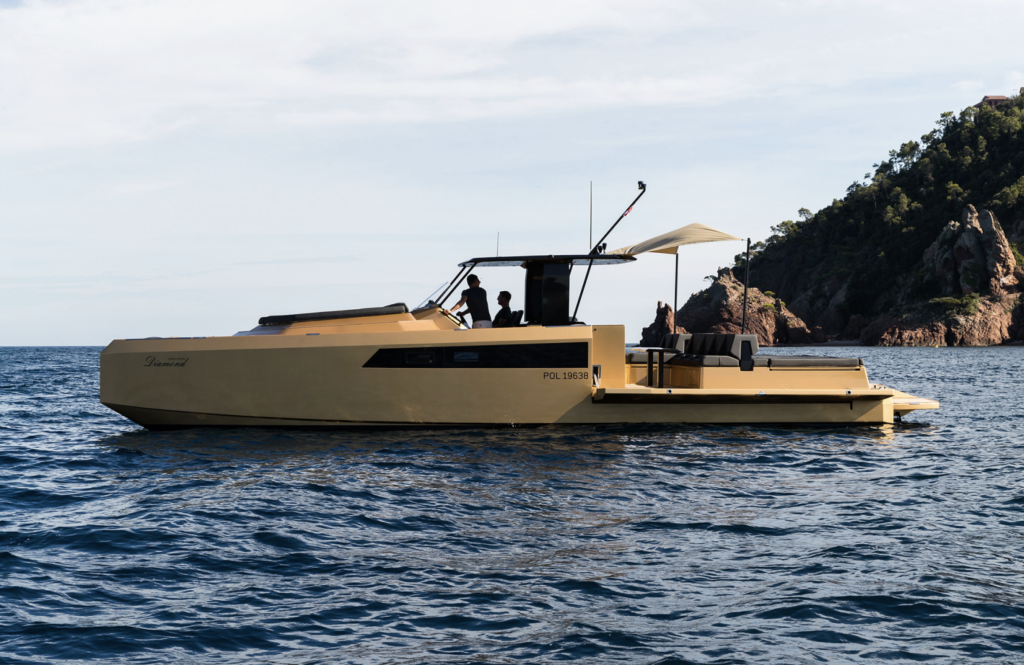 A luxury yellow yacht by Sunreef Yachts cruising on the calm sea, with a rocky shoreline in the background.