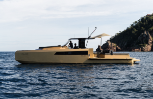 A luxury yellow yacht by Sunreef Yachts cruising on the calm sea, with a rocky shoreline in the background.