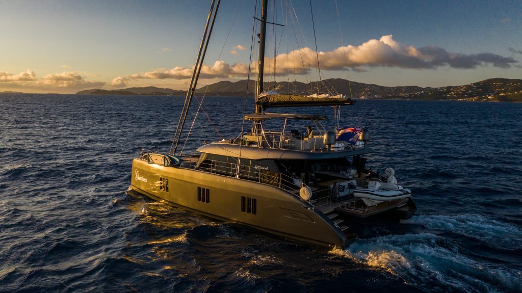 A luxurious Sunreef Yachts catamaran sails on the ocean under a warm sunset, with an island in the background.