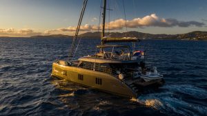 A luxurious Sunreef Yachts catamaran sails on the ocean under a warm sunset, with an island in the background.