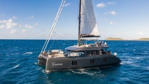 A luxury catamaran sailing in open water with the name 'Gracious' on its side. The yacht is manufactured by Sunreef Yachts and has spacious decks under a clear blue sky.