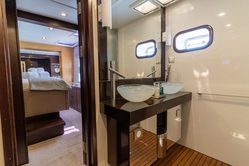 Interior of a Sunreef Yachts catamaran, showing a modern bathroom with glass sinks and a view into a bedroom with a cozy bed.