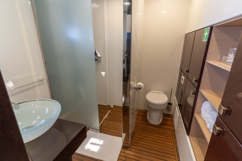 The interior of a modern yacht bathroom from Sunreef Yachts, featuring a glass basin, wooden floor, a toilet, and shelves with towels.