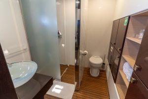 The interior of a modern yacht bathroom from Sunreef Yachts, featuring a glass basin, wooden floor, a toilet, and shelves with towels.