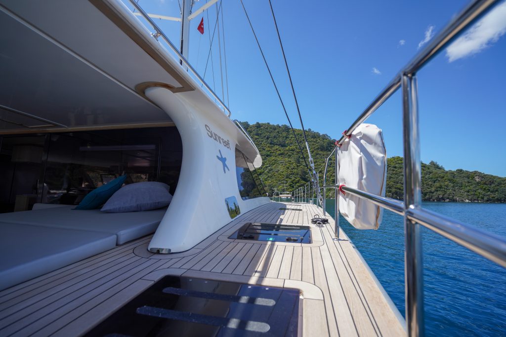 The deck of a Sunreef Yachts catamaran featuring sleek, modern design with cushioned seating and clear skies in the background.