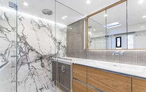 A luxurious bathroom on a Sunreef Yachts vessel featuring a modern design with a large marble-patterned wall, a spacious glass shower enclosure, a sleek double sink with wooden cabinetry, and a large mirror.