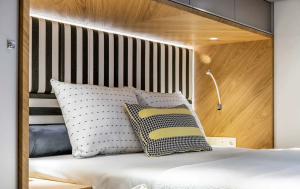 The image shows a luxurious bedroom interior aboard a Sunreef Yachts vessel, featuring a modern design with wooden accents, a bed with decorative pillows, and ambient lighting.
