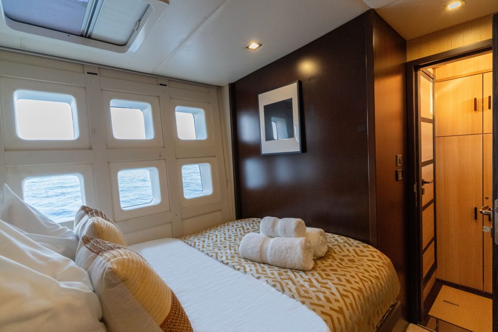 Interior view of a Sunreef Yachts cabin featuring a luxurious bed with patterned pillows and towels. Large windows offer a view of the sea, and there's a modern, elegant design with a framed picture on the wall.