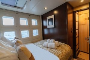 Interior view of a Sunreef Yachts cabin featuring a luxurious bed with patterned pillows and towels. Large windows offer a view of the sea, and there's a modern, elegant design with a framed picture on the wall.