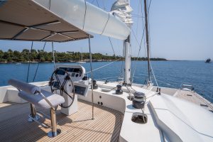 The deck of a Sunreef Yachts catamaran with a steering wheel and navigational instruments overlooking a serene blue sea and distant coastline.