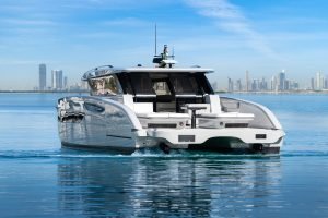 A sleek Sunreef Yachts catamaran on the water with a city skyline in the background, under a clear blue sky.