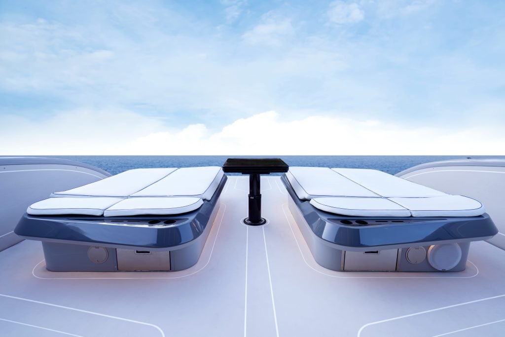 The image shows the deck of a luxury yacht from Sunreef Yachts with two sunbeds facing the ocean, under a clear blue sky.