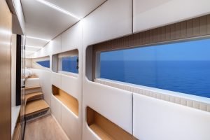 The interior hallway of a luxurious Sunreef Yachts catamaran features sleek, modern design with light wood and white paneling. Large windows on one side offer a clear view of the ocean.