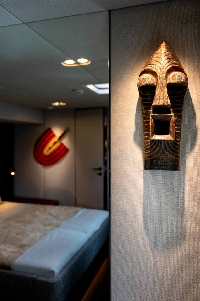 Interior of a luxury yacht from Sunreef Yachts, featuring a modern bedroom with a tribal mask mounted on the wall.