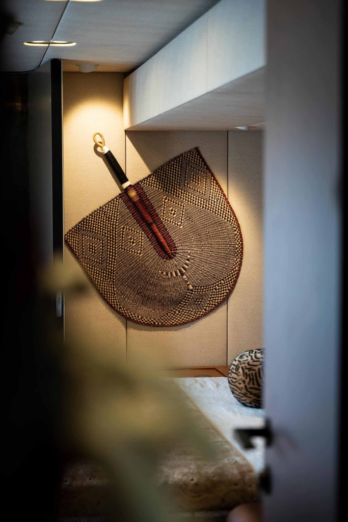The image shows the interior of a Sunreef Yachts vessel, featuring a decorative woven wall hanging, a circular patterned cushion, and a stylish, modern ambiance.