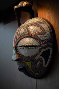 A decorative mask with intricate beadwork hangs on a wooden wall inside a Sunreef Yachts interior.